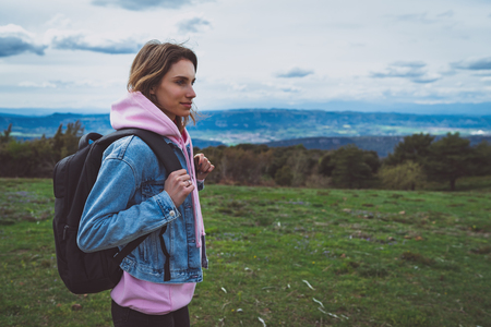 tourist traveler with black backpack standing on green top on mountain, hiker looking on hills and mountain, girl enjoying nature panoramic landscape in trip, relax holiday concept in trekking tripの写真素材