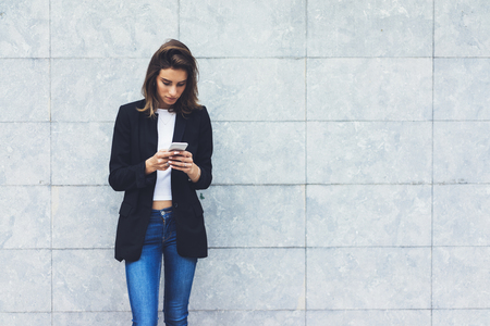 Portrait young businesswomen in black suit using smartphone isolated on background concrete gray wall mockup, pretty hipster manager holding mobile gadget, girl smiletexting message, connectの写真素材