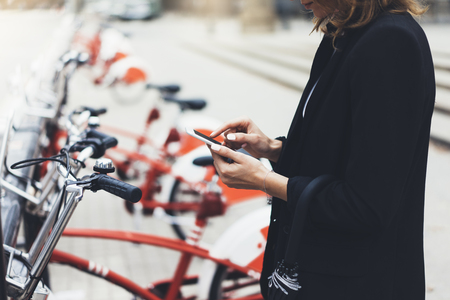 Young businesswomen in black  suit and umbrella using smartphone, biking and going to work by city bicycle on urban street, hipster girl holding mobile gadget, ecology environment conceptの写真素材