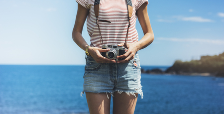 Tourist traveler photographer making pictures seascape on vintage photo camera on background yacht and boat piar, hipster girl enjoying peak mountain and nature holiday, mockup ocean waves view, blurred backdropの写真素材