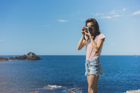 Tourist traveler photographer making pictures sea scape on vintage photo camera on background yacht and boat piar, hipster girl enjoying peak mountain and nature holiday, mockup ocean waves view, blurred backdropの写真素材