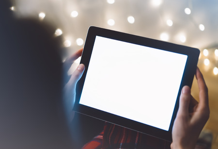 Hipster girl using tablet technology in home atmosphere, person holding computer on background glow bokeh Christmas illimination, female hands texting on relax glitter xmas decoration, mockup templates, blurの写真素材