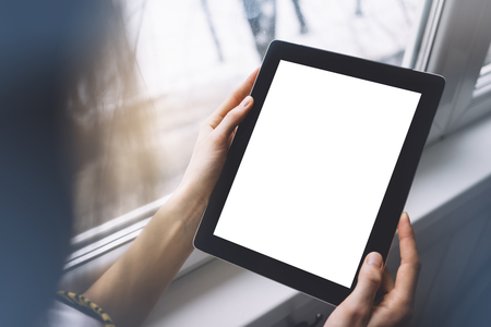 Hipster person hands holding digital tablet with empty blank screen, against a background of  window horizontal,  freelancer girl using at home on a computer on the balcony, mockup teghnology,  blurの写真素材