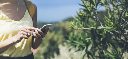 Hipster young girl with bright backpack looking at phone and map. Said view tourist traveler on background mountain, blue sea. Mock up for text message. Female hands using smartphone, holding gadgetの写真素材