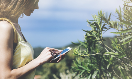 Hipster young girl with bright backpack looking at phone. Said view tourist traveler on background mountain, sea. Mock up for text message. Female hands using smartphone, holding gadgetの写真素材