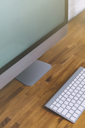Top view of a computer monitor with a blank screen on a pure white background of a brick wall and a keyboard on a wooden table, blank for your text or content or design, closeup. Mockup top viewの写真素材