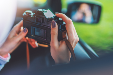 tourist girl in an open window of a auto car taking photography click on retro vintage photo camera crop, photographer looking on camera closeup technology, blogger hobby content conceptの写真素材