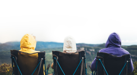 three friends sit in camping chairs on top of a mountain, travelers enjoy nature, tourists look into distance on background of panoramic landscape, weekend concept, mockupの写真素材