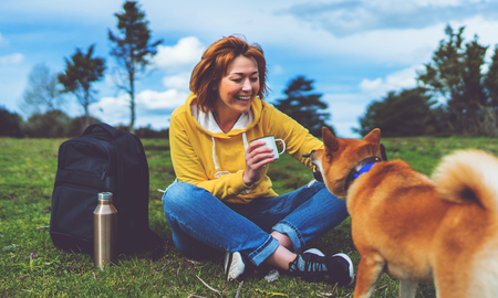 Happy girl with smile drink cup playing with red japanese dog shiba inu on green grass in the outdoors nature park, beautiful young woman hipster and dog friends, friendship lifestyle conceptの写真素材