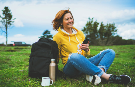 woman relax holding in female hands gadget technology, tourist young girl on background green grass using mobile smartphone, smile hiker enjoy recreation, online wifi internet lifestyle conceptの写真素材