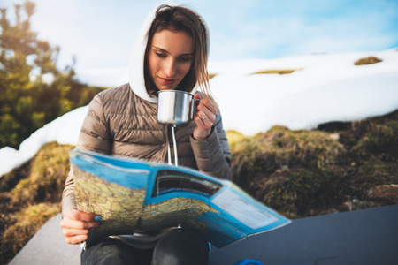 girl hold in hands cup of drinks, relax tourist look on map, people planning trip in snow mountain, hipster enjoy on background winter nature, lifestyle holiday concept, journey landscape tripの写真素材