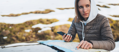 girl hold in hands mobile phone and looking on map, relax tourist travels by auto car, people planning trip in snow mountain, hipster enjoy winter nature, journey landscape trip, lifestyle holiday conceptの写真素材