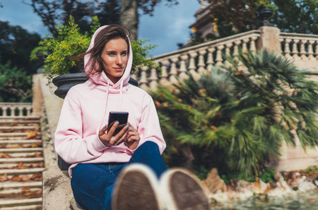 girl hold in hands mobile phone, person type message on smartphone, relax tourist travels planning trip in sun city, hipster enjoy journey in cityscape, lifestyle holiday conceptの写真素材