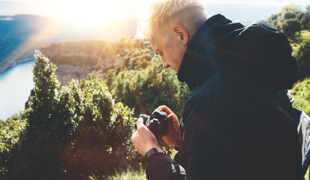 hipster tourist hold in hands taking photography click on retro vintage photo camera in auto, photographer looking on camera technology, blogger using hobby content concept, sun flare mountain, panoramic landscapeの写真素材
