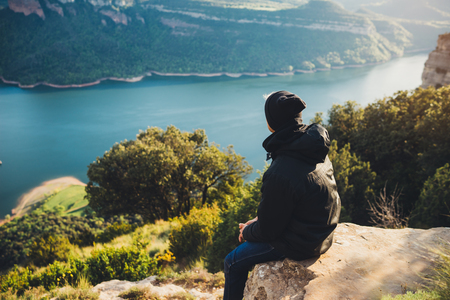 tourist traveler sits on top mountain and enjoys river, hiker relax looking on blue sky clouds, background nature panoramic landscape in trip, holiday mockup concept in trekking tripの写真素材