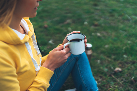 Happy girl holding in hands cup of hot tea on green grass in outdoors nature park top view, beautiful woman hipster enjoy drinking cup of coffee, lifestyle relax recreation meditation conceptの写真素材