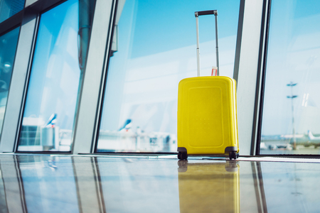 isolate traveler tourist yellow suitcase at floor airport on background large window, bright luggage waiting in departure lounge area hall of âairport lobby terminal, vacation trip concept, empty space mockupの写真素材