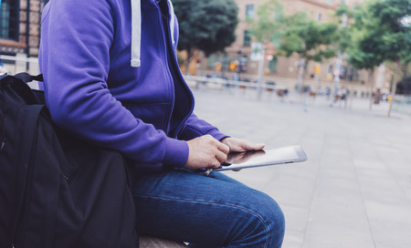 Hipster texting message on tablet computer or technology blank screen mockup. Smile young man using digital on building castle background. Male hands tourist holding gadget on blur cityscapeの写真素材
