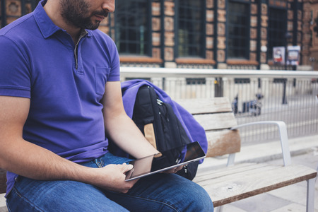 Hipster texting message on tablet computer or technology screen mockup. Smile young man using digital on building castle background. Male hands tourist holding gadget on blur cityscapeの写真素材