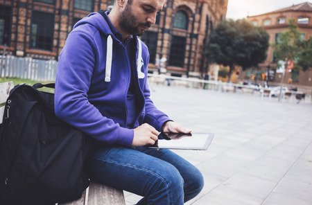 Hipster texting message on tablet computer or technology screen mockup. Smile young man using digital on building castle background. Male hands tourist holding gadget on blur cityscapeの写真素材