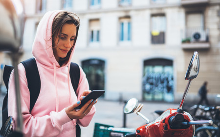 girl hold in hands mobile phone, person type message on smartphone, tourist traveler planning trip on moto scooter, hipster enjoy journey in cityscape, lifestyle holiday concept, internet onlineの写真素材