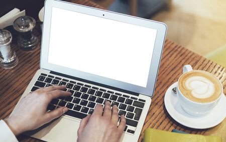 Woman writing text on open laptop on wood table with empty blank screen monitor at home, person drink cup of coffee on background atmosphere cafe, female hands working on computer, mockup templatesの写真素材