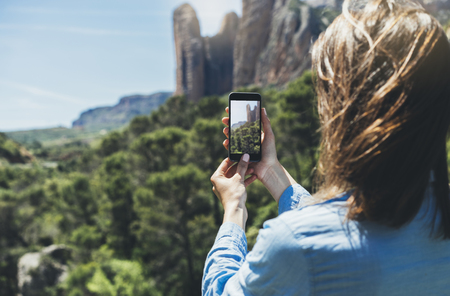Hipster girl making photo on smartphone mobile closeup, view tourist hands using gadget phone in travel on background mountains and sky landscape; finger touch screen cellphone mockup nature, templatesの写真素材