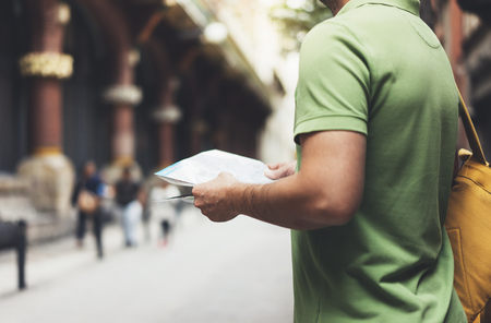 Hipster young man with backpack looking and holding map. Said view tourist traveler planning route on background sun city. Person visiting the sights Barcelona. Mockup, backdrop summer streetの写真素材