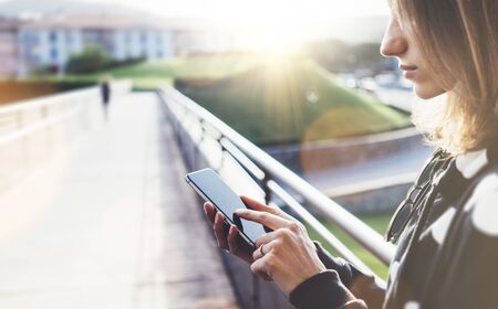 Hipster texting message on smartphone or technology, mock up of blank screen. Tourist girl using cellphone on bridge background close. Female hands holding gadget on blurred backdrop. Mockup copy space for text message or designの写真素材