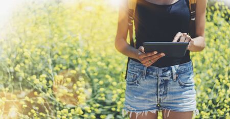 Hipster texting message on tablet or technology, mock up of blank screen. Girl using computer on yellow flowers background close. Female hands holding gadget on blurred backdrop. Mockup side view. Copy space for text message or designの写真素材