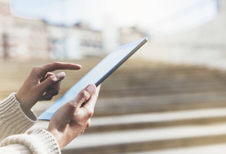 Hipster tourist texting message on tablet or technology mock up. Person using computer on building background close. Female hands holding gadget on blurred backdrop mockup. Copy space for text message or designの写真素材