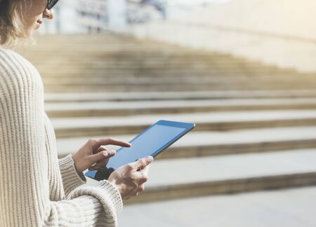 Hipster tourist texting message on tablet or technology mock up. Person using computer on building background close. Female hands holding gadget on blurred backdrop mockup. Copy space for text message or designの写真素材