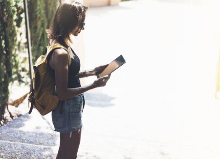 Hipster young girl with bright backpack and vintage camera using tablet or holding gadget, planning travel plan. View tourist traveler with sunglasses on background Parc Laberint Barcelona. Mock up for text messageの写真素材