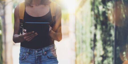 Hipster young girl with bright backpack and vintage camera using tablet or holding gadget, planning travel plan. View tourist traveler with sunglasses on background Parc Laberint Barcelona. Mock up for text messageの写真素材