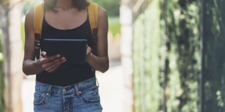 Hipster young girl with bright backpack and vintage camera using tablet or holding gadget, planning travel plan. View tourist traveler with sunglasses on background Parc Laberint Barcelona. Mock up for text messageの写真素材