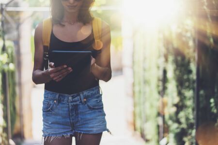Hipster young girl with bright backpack and vintage camera using tablet or holding gadget, planning travel plan. View tourist traveler with sunglasses on background Parc Laberint Barcelona. Mock up for text messageの写真素材