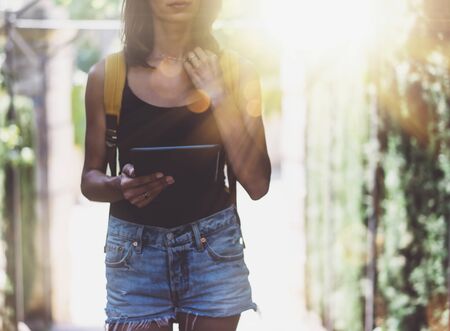 Hipster young girl with bright backpack and vintage camera using tablet or holding gadget, planning travel plan. View tourist traveler with sunglasses on background Parc Laberint Barcelona. Mock up for text messageの写真素材