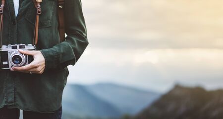 Hipster young girl with bright backpack taking photo of amazing landscape sunset on vintage camera close on peak of foggy mountain mockup. Tourist traveler on background sunlight in trip in northern spain basque country, mock up for text.の写真素材