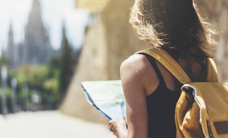 Hipster young girl with bright backpack and fashion sunglasses looking at map. Said view tourist traveler on background sun city. Person visiting the sights Barcelona. Mock up for text message.の写真素材