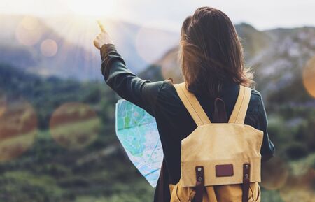 Hipster young girl with bright backpack enjoying sunset on peak of foggy mountain, looking a map and poining hand. Tourist traveler on background valley landscape panoramic view mockup, sunlight in trip in northern spain basque country, mock up for text.の写真素材