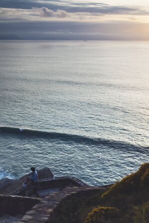 Young hipster relax on the beach on background ocean sunrise, silhouette romantic person looking view evening seascape, girl enjoy sunset on coast, travel holidays vacation, back figure on backdrop seaの写真素材