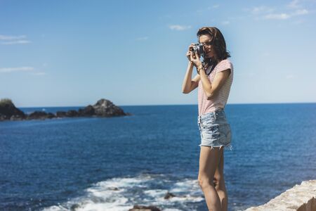 Tourist traveler photographer making pictures sea scape on vintage photo camera on background yacht and boat piar, hipster girl enjoying peak mountain and nature holiday, mockup ocean waves view, blurred backdropの写真素材