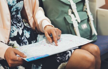 Enjoying travel. Young pretty woman traveling by train sitting near the window pointing finger and looking map. Tourist texting online message and plan route of railway, railroad transport conceptの写真素材