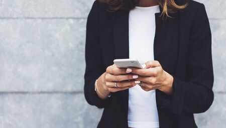 Portrait young businesswomen in black suit using smartphone isolated on background concrete gray wall mockup, pretty hipster manager holding mobile gadget, girl smiletexting message, connectの写真素材