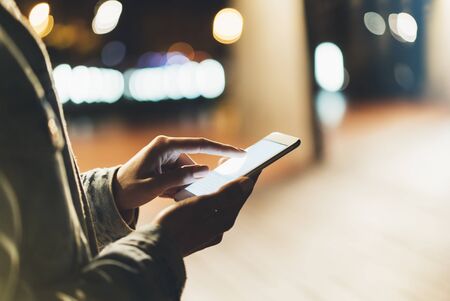 Girl pointing finger on screen smartphone on background illumination bokeh color light in night atmospheric city, hipster using in female hands and texting mobile phone, mockup glitter street, content lifestyleの写真素材