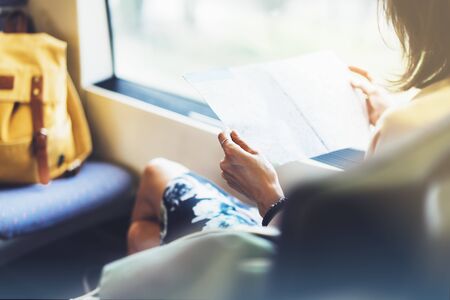 Enjoying travel. Young pretty woman traveling by train sitting near the window using smartphone and looking map. Tourist texting online message and plan route of railway, railroad transport conceptの写真素材