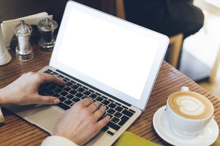 Woman writing text on open laptop on wood table with empty blank screen monitor at home, person drink cup of coffee on background atmosphere cafe, female hands working on computer, mockup templatesの写真素材