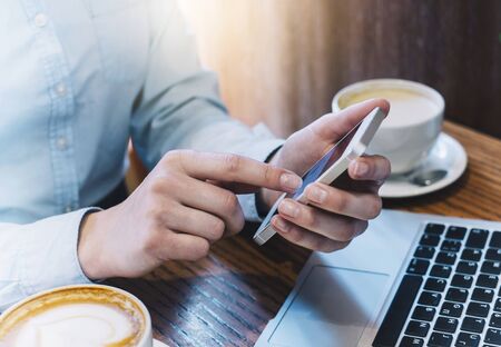 Girl pointing finger smartphone, hipster using open laptop with empty blank monitor screen in office, cup of coffee on background bokeh of light in cafe, female hands texting on mobile mockup, blurの写真素材