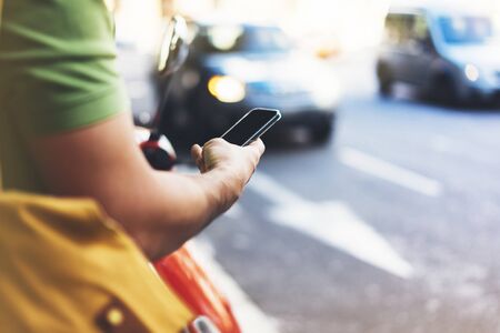 Man pointing on screen smartphone on background cars, tourist hipster waiting using in hands mobile phone, traveler connect wifi internet and calls taxi, headlights auto on backdrop city street, mockupの写真素材