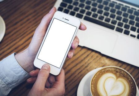 Girl pointing finger smartphone, hipster using open laptop with empty blank monitor screen in office, cup of coffee on background bokeh of light in cafe, female hands texting on mobile mockup templates, blurの写真素材